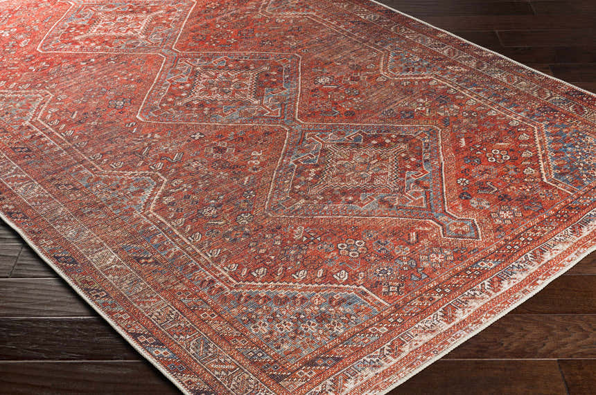 Close-up of the Siocon Washable Area Rug. Farmhouse style rug with traditional pattern in red, blue, and cream on dark wood floors. Corner