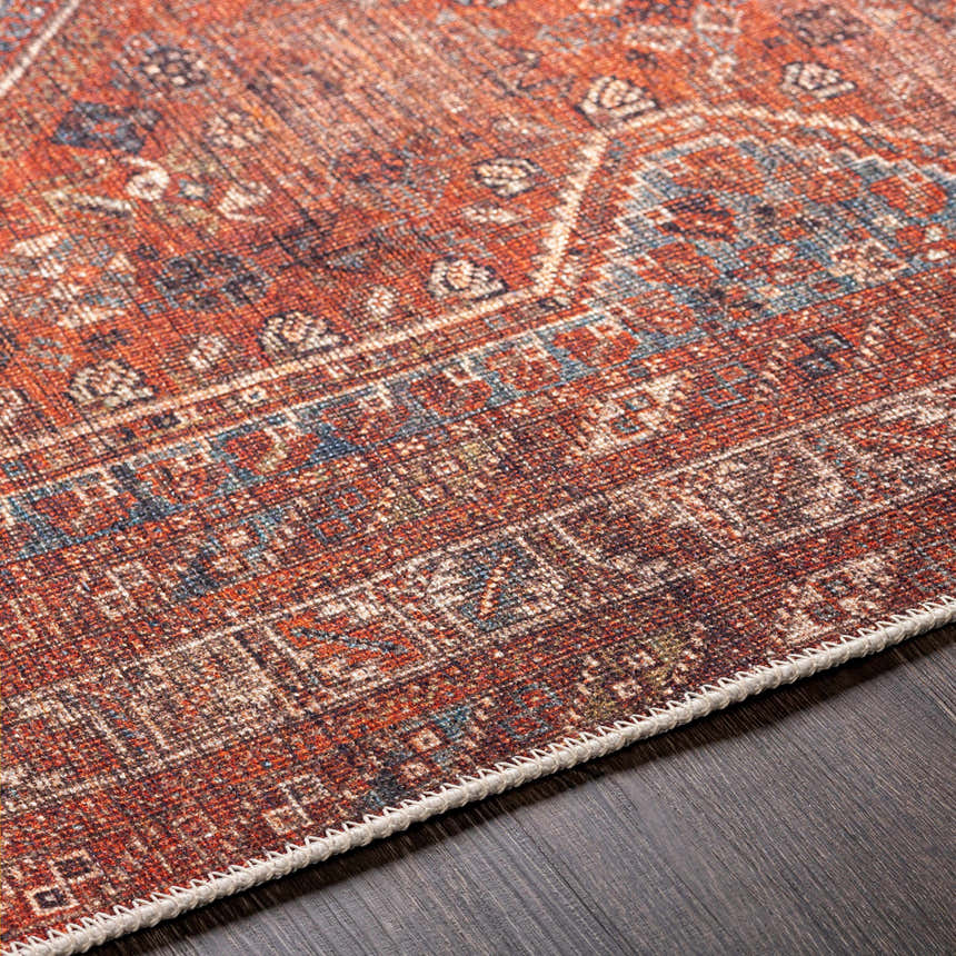 Close-up of the Siocon Washable Area Rug. Farmhouse style rug in rust, blue, and cream with a traditional pattern and woven texture. Texture