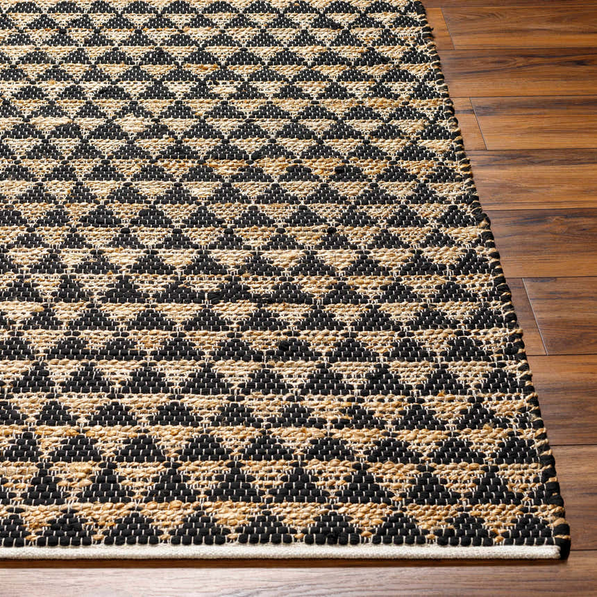 Close-up of the hand woven Colm Recycled Black Jean Rug, featuring a geometric black and jute pattern on a wood floor. Front