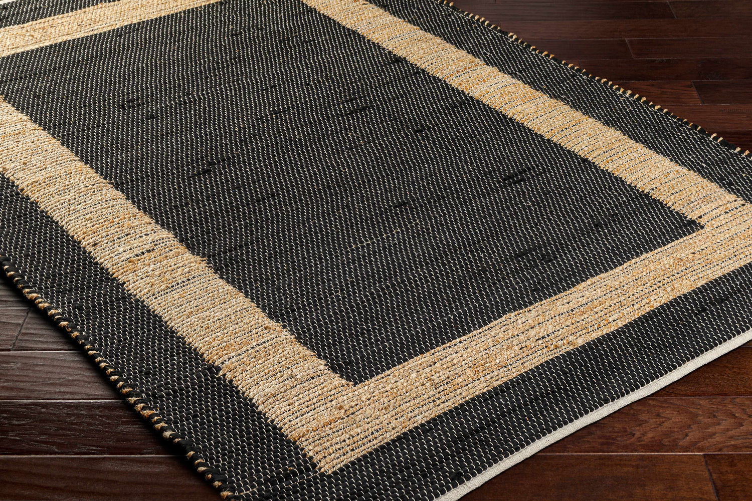 Close-up of the hand woven Ghita Black Area Rug showing its black and tan border design and texture. Corner
