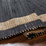 Close-up of the hand woven Ghita Black Area Rug showing black and tan braided texture on wood floor. Fold