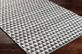 Close-up of the Gzifa Jute Rug showing a black and white houndstooth pattern and hand woven texture. Corner