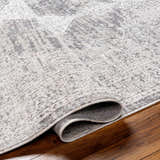 Close-up of the Azibo Area Rug showing its light gray, taupe, and black traditional pattern and recycled fabric texture. Fold