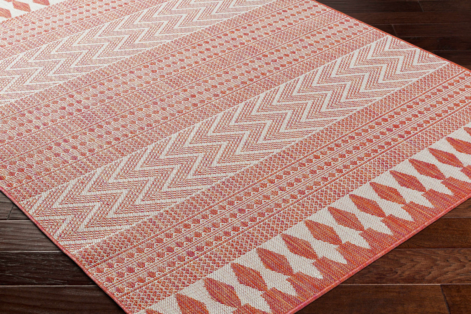 Close-up of the Asif Orange Area Rug showing its geometric, zigzag, and diamond patterns in terracotta and cream. Corner