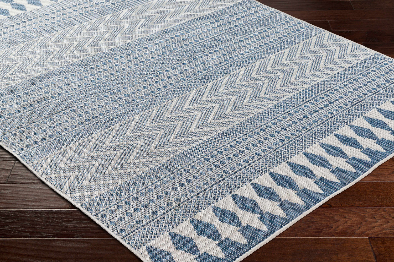 Close-up of the Asif Blue Area Rug showing a farmhouse style geometric pattern in denim and silver gray on a dark wood floor. Corner