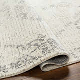 Close-up of the Tait Area Rug showing its bone color, subtle dark gray pattern, and soft, textured pile. Fold
