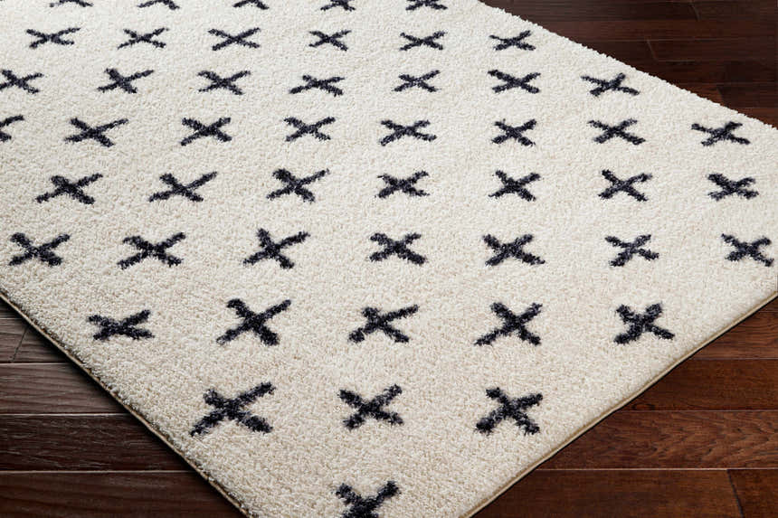 Close-up of the Bede Washable Area Rug. Beige shag rug with a charcoal geometric X pattern. Transitional style. Corner