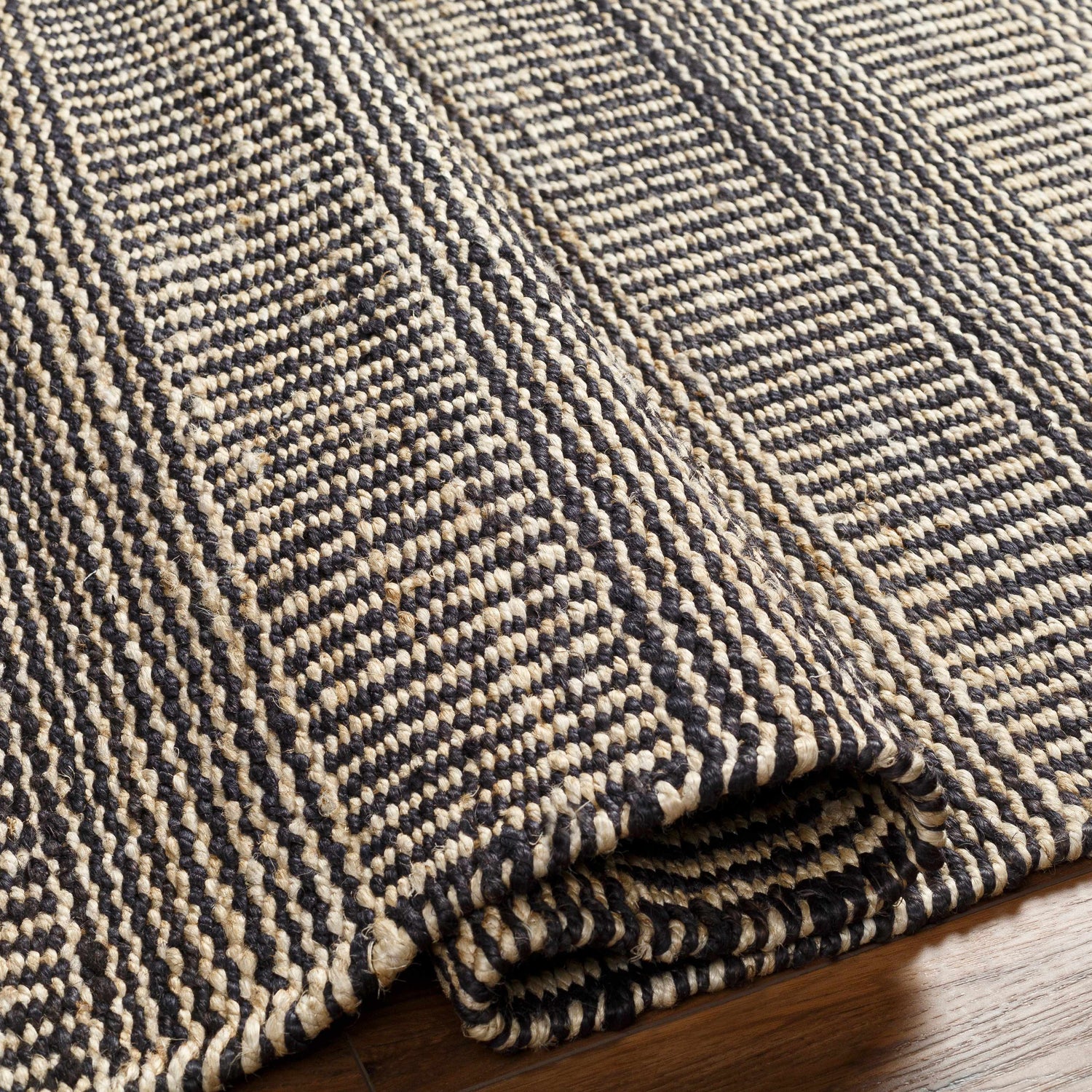 Close-up of the hand-woven Black Elle Area Rug. Features a geometric pattern in black and natural jute. Scandinavian, Southwestern style. Fold