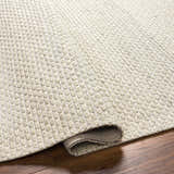 Close-up of the hand woven Cream Emlen Area Rug showing the textured wool design and rolled edge on a wood floor. Fold