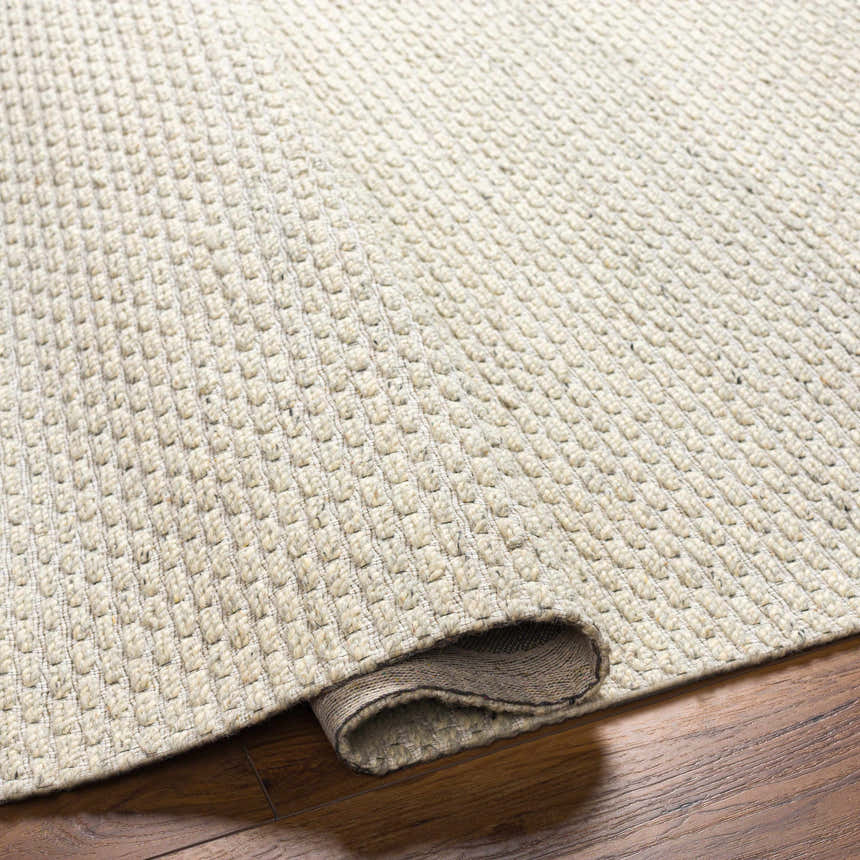Close-up of the hand woven Cream Emlen Area Rug showing the textured wool design and rolled edge on a wood floor. Fold