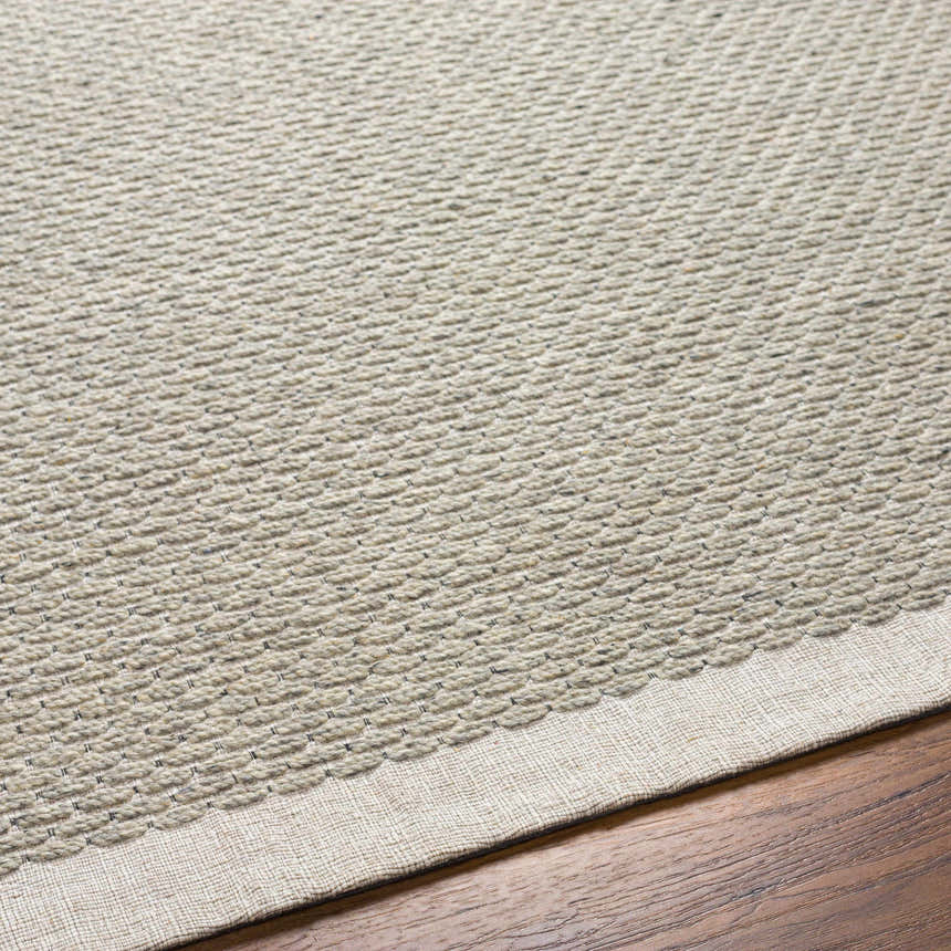 Close-up of the hand woven Light Brown Emlen Area Rug showing its textured wool design and cream color on a wood floor. Texture