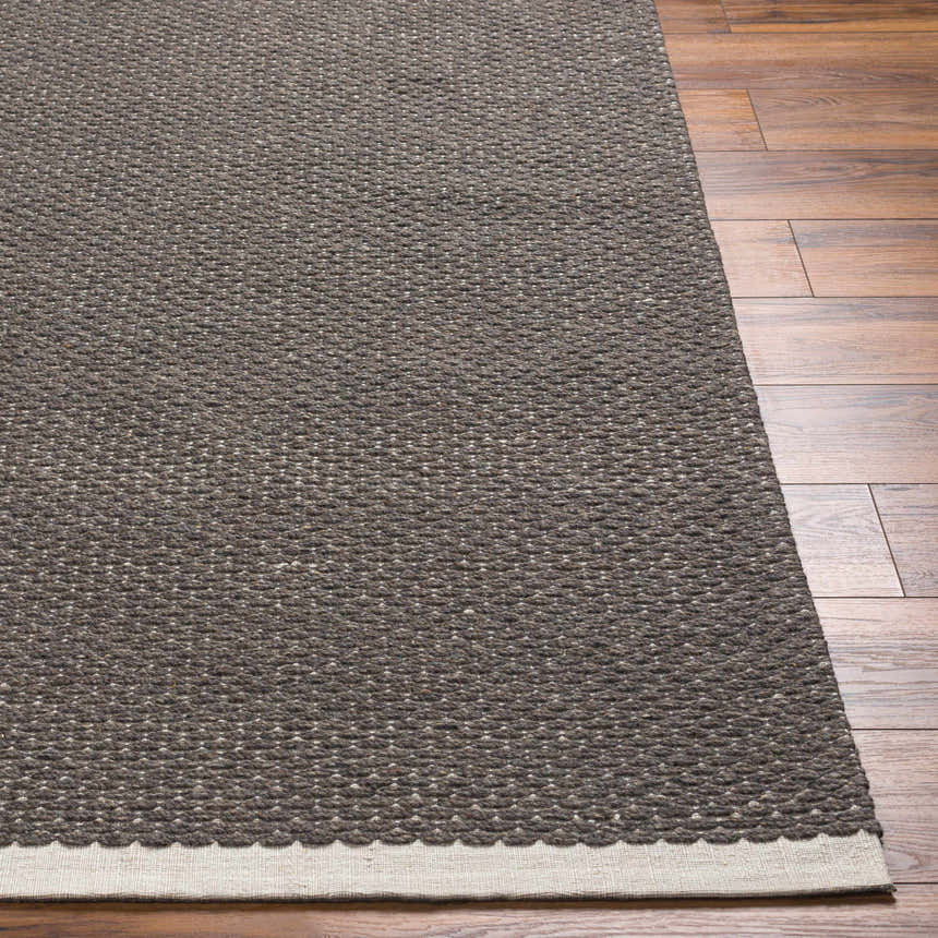 Close-up of the hand woven Emlen Nutmeg Area Rug showing its wool texture, nutmeg color, and beige border on wood floors. Front