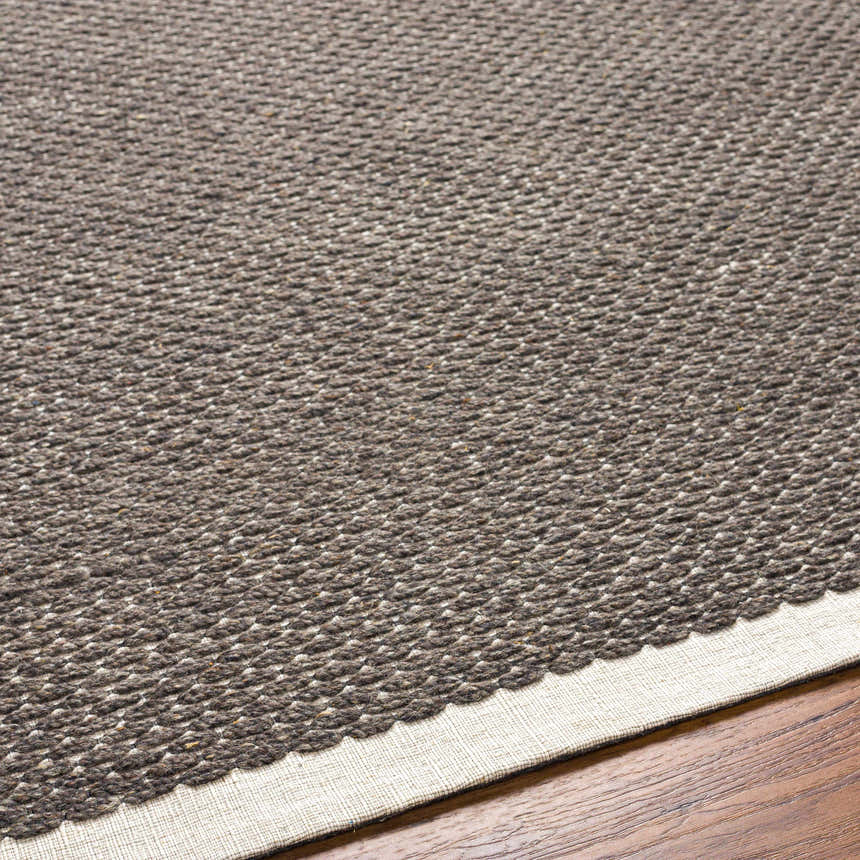 Close-up of the hand-woven Emlen Nutmeg Area Rug showing its textured wool and beige border on a wood floor. Texture