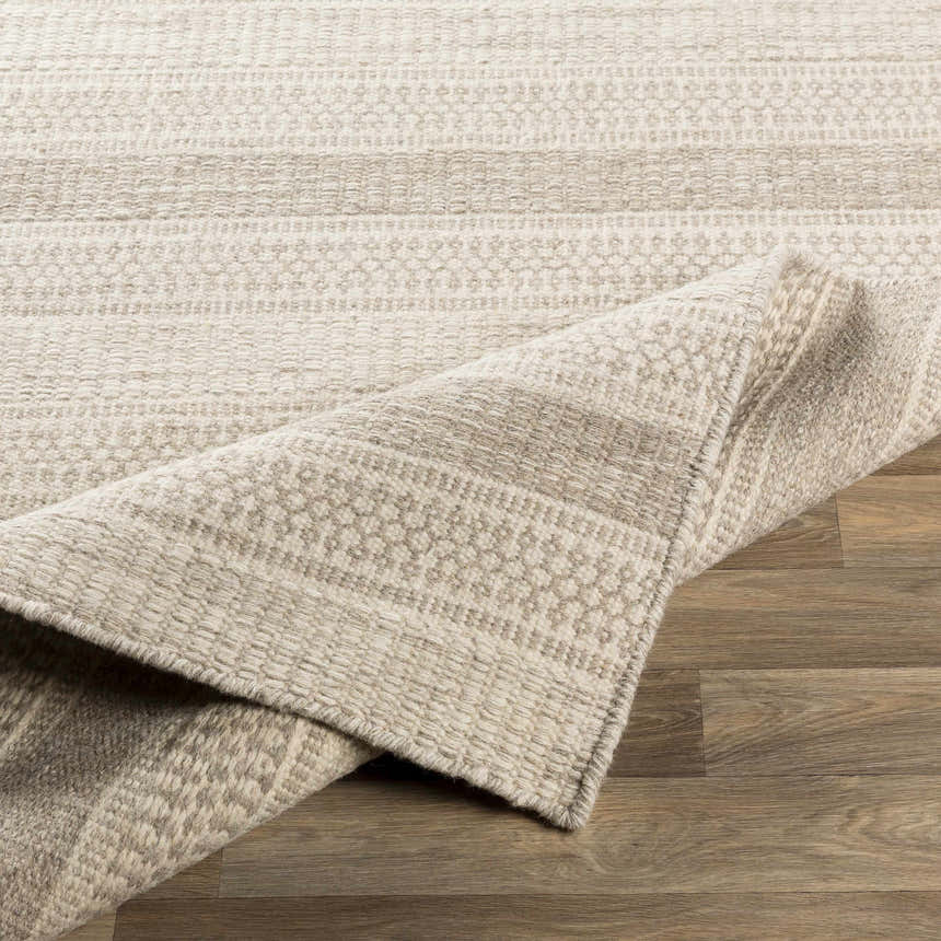 Close-up of the Silverthorne Wool Area Rug. Cream and gray rug with a textured, hand-woven design on wood floor. Fold