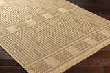 Close-up of the Gerik Faux Jute Rug. Light brown rug with a subtle geometric pattern and textured weave. Farmhouse style. Corner
