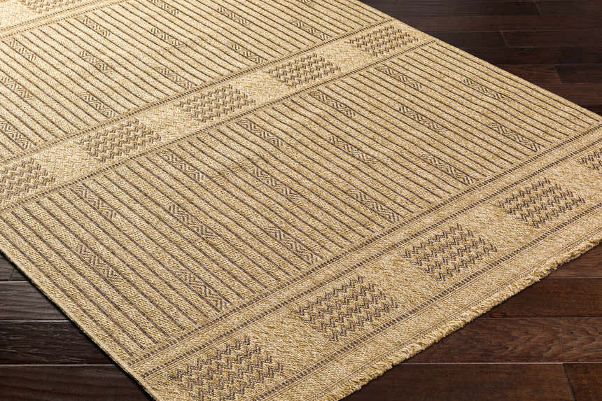 Close-up of the Gerik Faux Jute Rug. Light brown rug with a subtle geometric pattern and textured weave. Farmhouse style. Corner