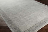 Close-up of the hand-knotted Petra 2x3 Carpet in dark brown, light gray, medium gray, and taupe on a dark wood floor. Corner