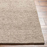Close-up of the hand-woven Alyra Tan Solid Area Rug on a wood floor, showing its neutral tan color and textured weave. Front