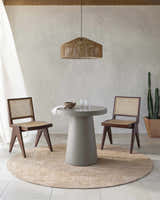 Dining room scene with a round Dekan Tan Area Rug, concrete table, and cane chairs. Roomscene-Round
