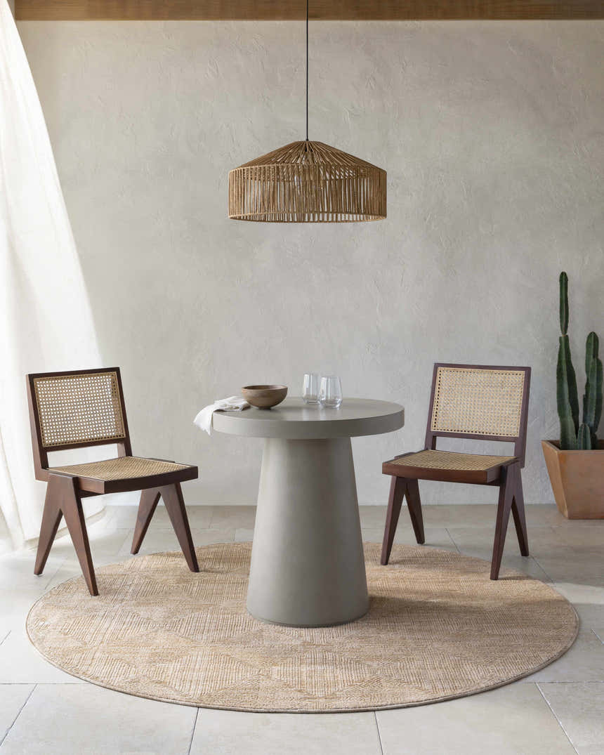 Dining room scene with a round Dekan Tan Area Rug, concrete table, and cane chairs. Roomscene-Round