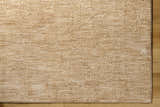 Close-up of the tan Kahua Area Rug showing its subtle texture and machine-woven construction on a wood floor. Corner