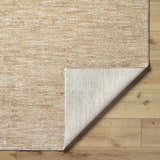 Close-up of the Kahua Tan Area Rug showing its neutral tan color, subtle texture, and the rug's backing on light wood floors. Fold