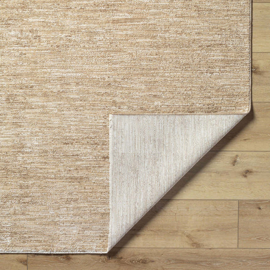 Close-up of the Kahua Tan Area Rug showing its neutral tan color, subtle texture, and the rug's backing on light wood floors. Fold
