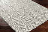 Close-up of Dawid Wool Area Rug with geometric black and bone triangle pattern on dark wood floor. Corner