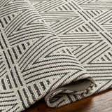 Close-up of the Dawid Wool Area Rug, showcasing its black and bone geometric pattern and hand-woven texture. Fold