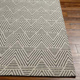 Close-up of the Dawid Wool Area Rug featuring a geometric black and off-white triangle pattern on hardwood floors. Front