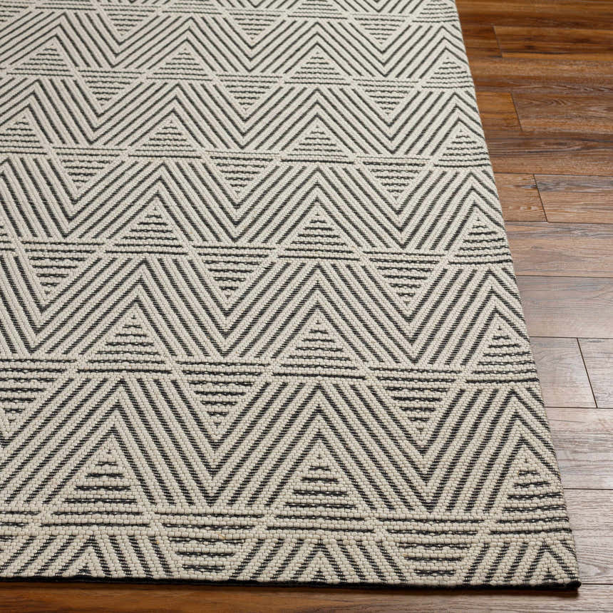 Close-up of the Dawid Wool Area Rug featuring a geometric black and off-white triangle pattern on hardwood floors. Front