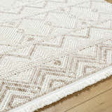 Close-up of the Armen Area Rug, a beige and cream rug with a geometric pattern and fringe detail. Texture