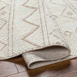 Close-up of the Armen Area Rug showing a geometric pattern in cream and beige on a textured, machine-woven surface. Fold