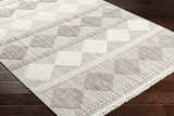 Close-up of the Igone Area Rug showing a beige and brown geometric block pattern with fringe on dark wood floors. Corner