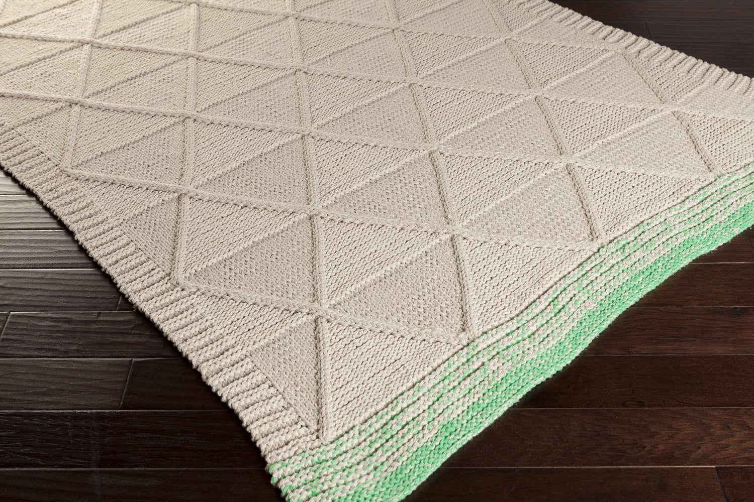 Close-up of the hand woven Snyder Area Rug. Features a geometric triangle pattern and green trim on dark wood floors. Corner