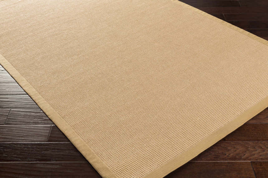 Close-up of the Nevis Jute Rug in mustard and natural jute, showing the hand-woven texture and tan border on dark wood floors. Corner