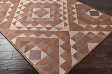 Close-up of the Somis Area Rug. Hand-crafted leather rug in black, camel, and gray geometric pattern on dark wood floor. Corner