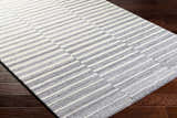 Close-up of Gawel Gray Area Rug showing gray and white stripes on dark wood floor. Contemporary style. Corner