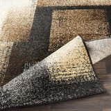 Close-up of the Spraggs Area Rug showing its geometric pattern in black, charcoal, brown, beige, and tan hues. Fold