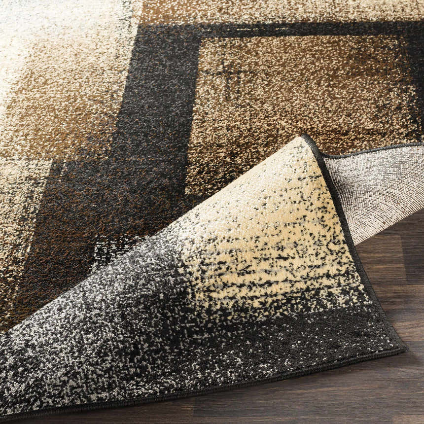 Close-up of the Spraggs Area Rug showing its geometric pattern in black, charcoal, brown, beige, and tan hues. Fold