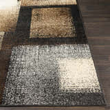 Close-up of the Spraggs Area Rug. Geometric pattern in black, charcoal, dark brown, gray, light beige, and tan. Machine woven texture. Front