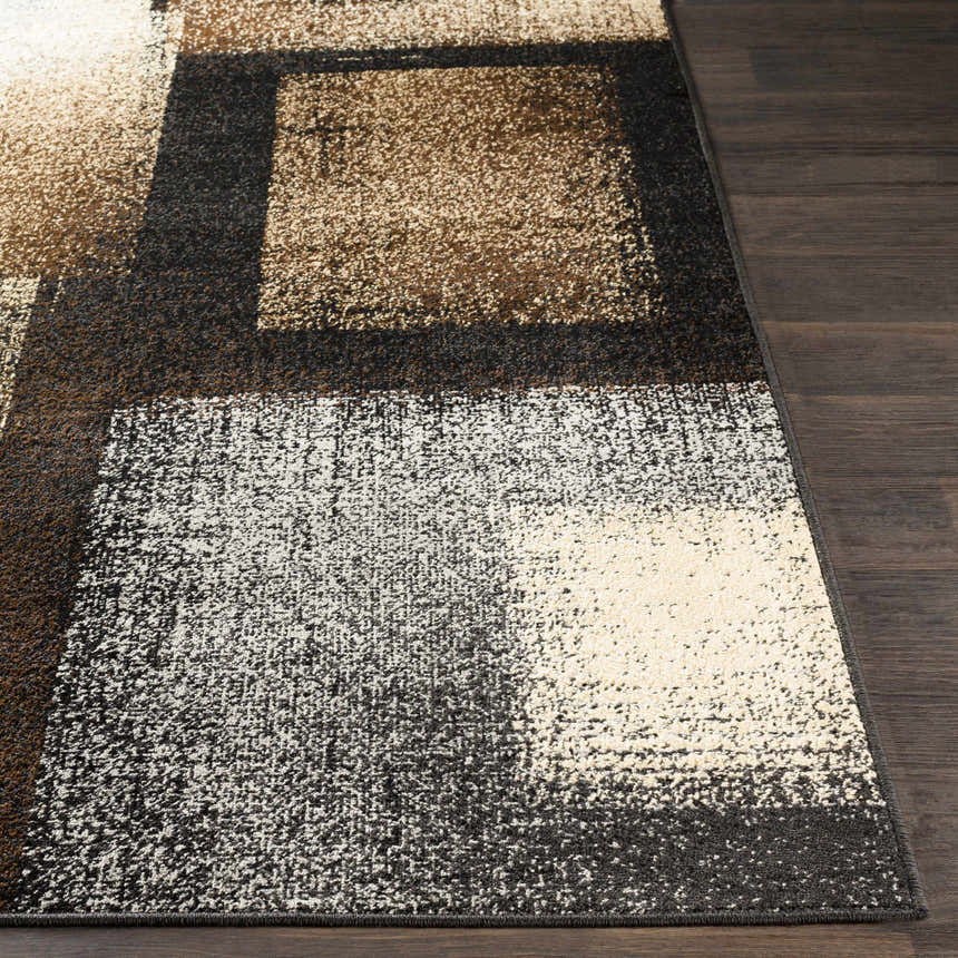 Close-up of the Spraggs Area Rug. Geometric pattern in black, charcoal, dark brown, gray, light beige, and tan. Machine woven texture. Front