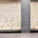 Close-up of Spraggs Area Rug texture. Beige rug with black, brown and gray spots. Ruler shows rug thickness. Pile