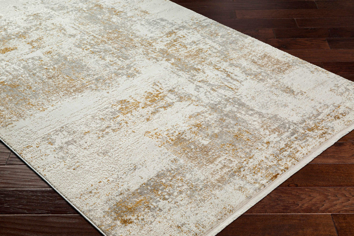 Close-up of Hatsu Area Rug showing beige, gray, and gold abstract pattern on a cream background and dark wood floor. Corner