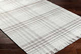 Close-up of the Inara Plaid Area Rug. Hand woven rug in dark gray, light gray, and silverton on dark wood floors. Corner