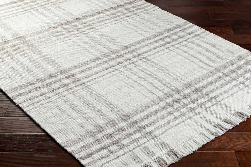 Close-up of the Inara Plaid Area Rug. Hand woven rug in dark gray, light gray, and silverton on dark wood floors. Corner