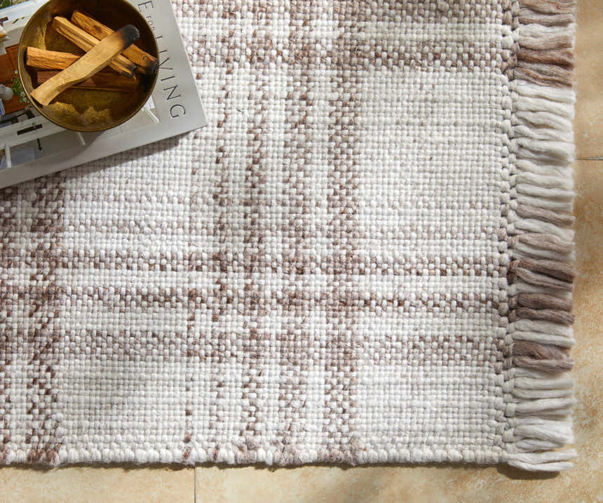 Close-up of the Inara Light Brown Plaid Hand Woven Area Rug, showing the beige and brown pattern and textured fringe. Styleshot