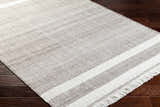 Close-up of the hand-woven Loic Light Brown Area Rug with white stripes and fringe detail on dark wood floors. Corner