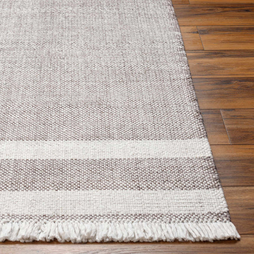 Close-up of the hand-woven Loic Light Brown Area Rug showing its texture, striped pattern, and fringe detail on wood floors. Front