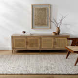 Living room scene with a beige Olisa Cream Wool Area Rug, wood cabinet, and modern chair. Roomscene-Rectangle